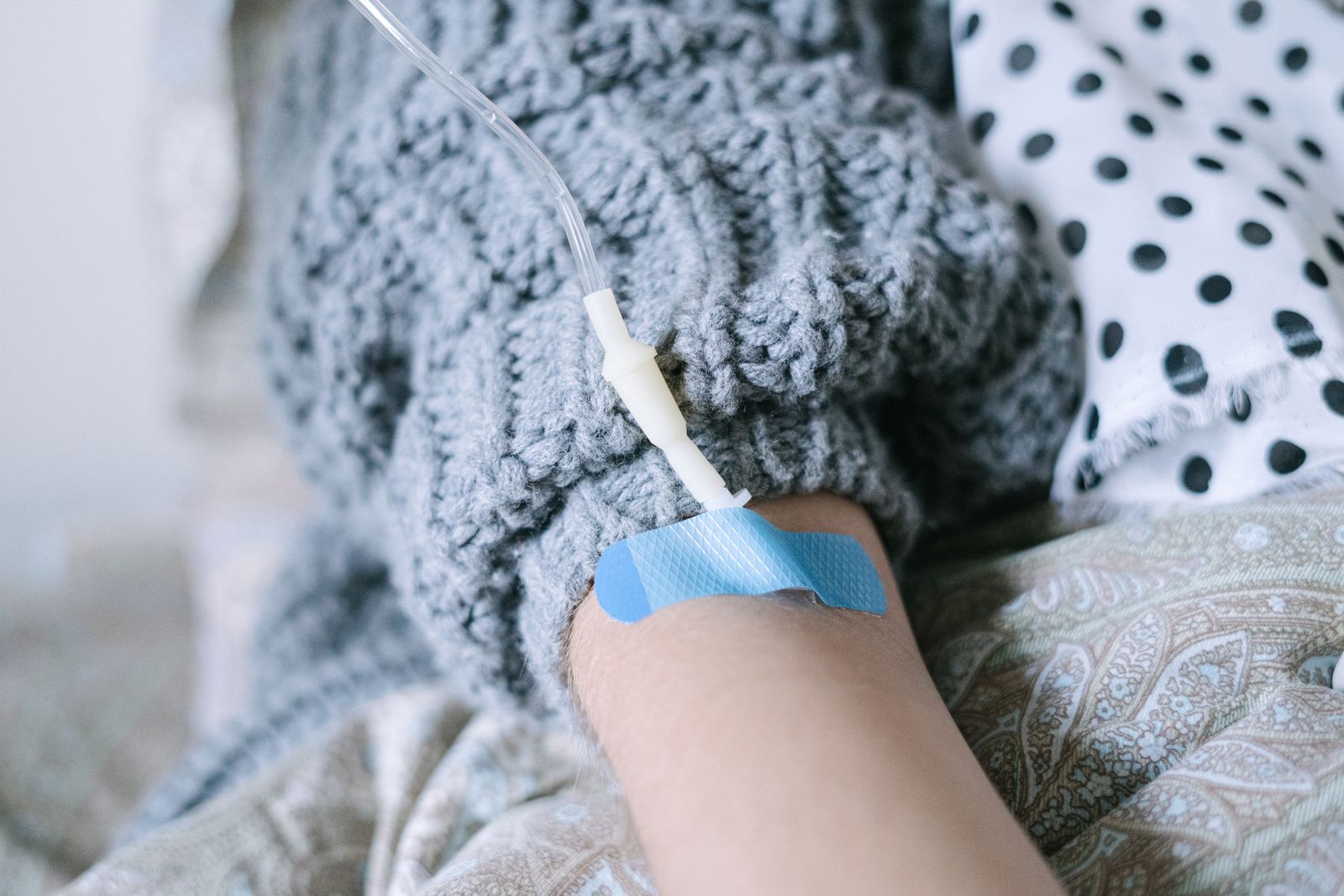 A person resting under a soft knit blanket while receiving an IV infusion